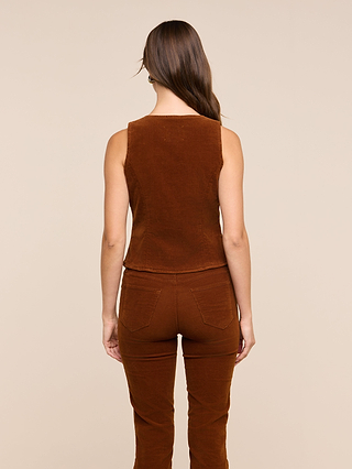 A woman with long brown hair is standing with her back to the camera, wearing the sleeveless tailored Yelena Vest and matching brown corduroy pants against a plain beige background.