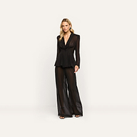A woman wearing a Rouvier Blazer Top with sheer fabric, statement shoulders, and a tailored waist, paired with matching wide-leg trousers.