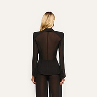 A woman viewed from behind wearing the black, sheer, long-sleeved Rouvier Blazer Top, featuring statement shoulders and structured button cuffs.