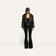 A person wearing a cropped black Vail Puffer jacket with an oversized collar, a black top, and black flared trousers.