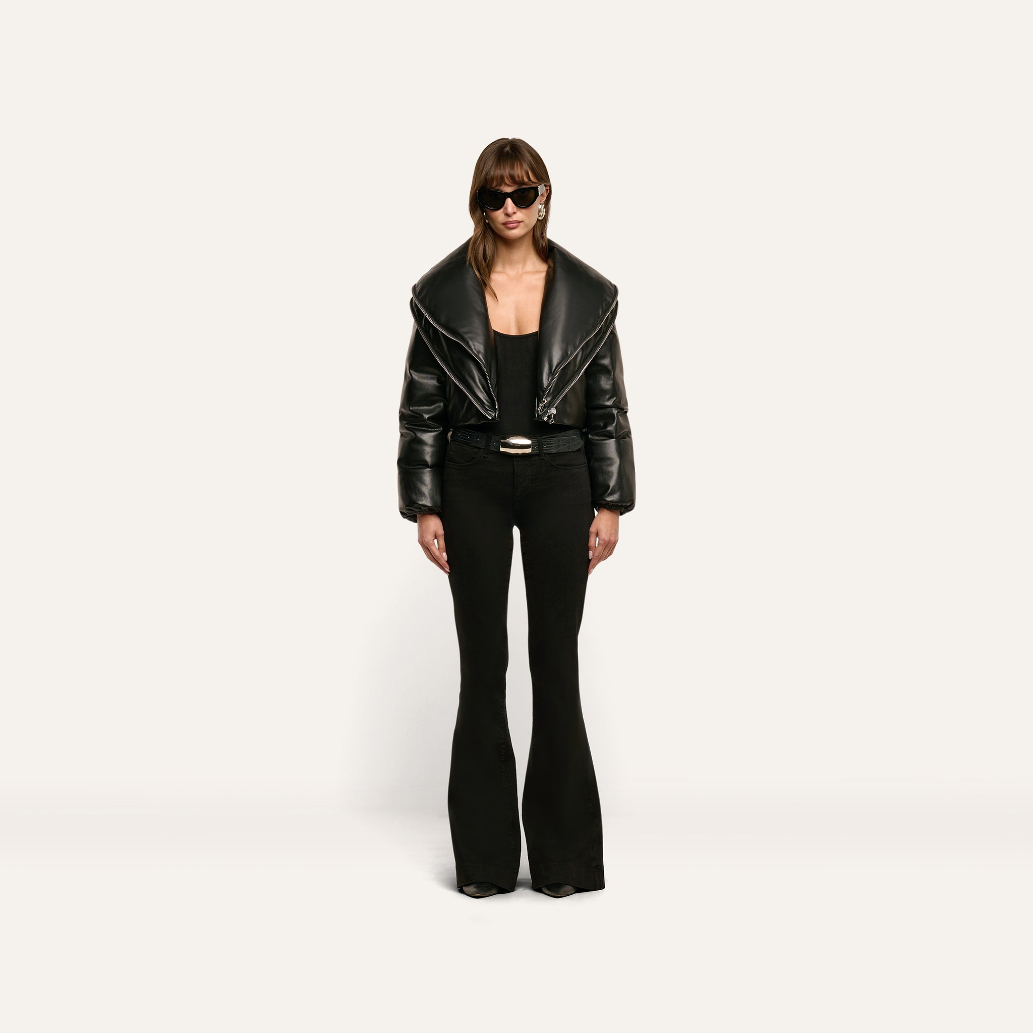 A person wearing a cropped black Vail Puffer jacket with an oversized collar, a black top, and black flared trousers.