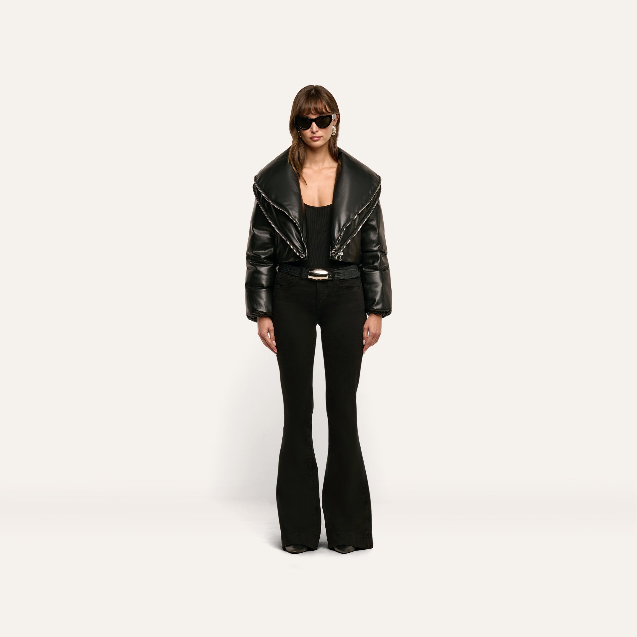 A person wearing a cropped black Vail Puffer jacket with an oversized collar, a black top, and black flared trousers.