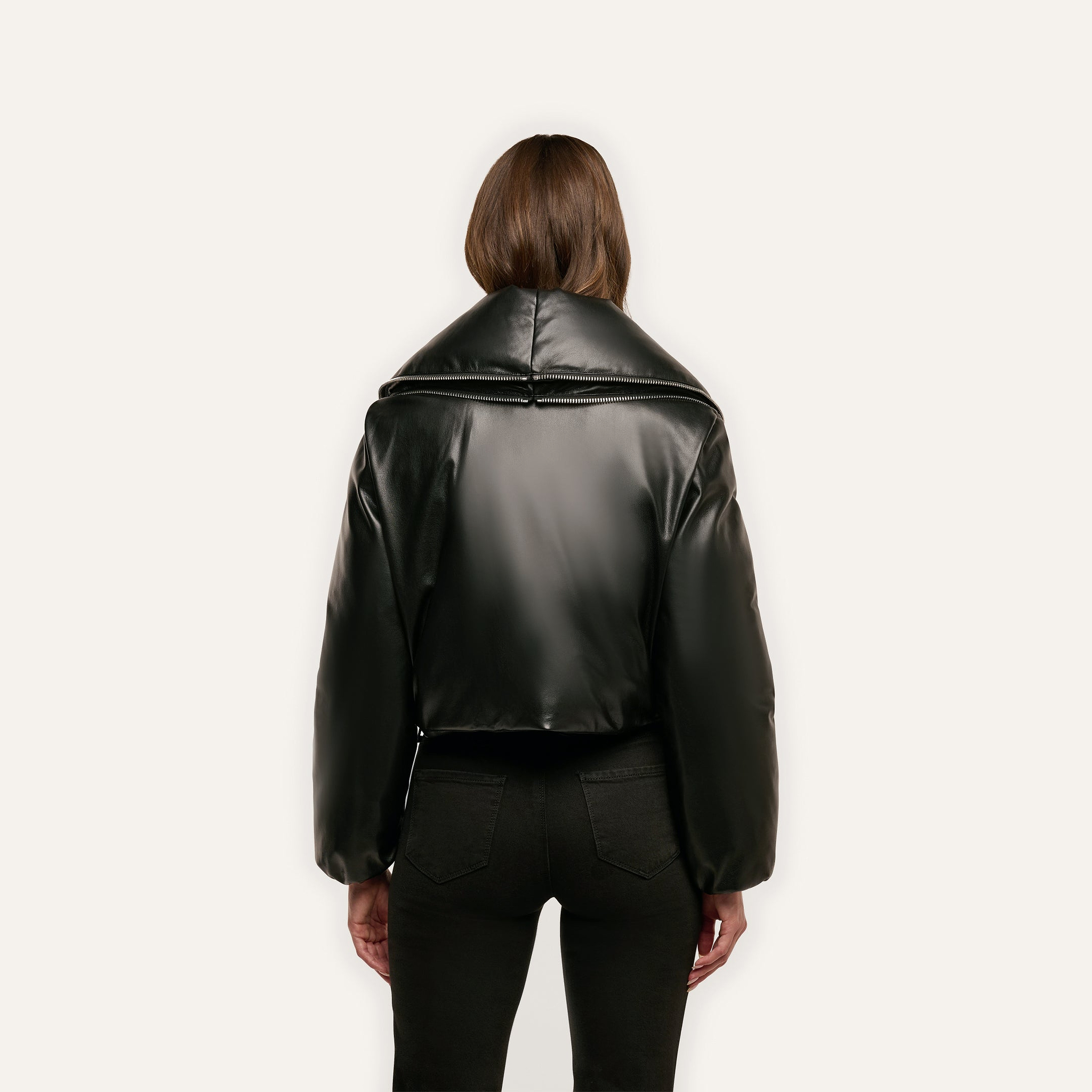 Back view of a person wearing a black cropped Vail Puffer jacket with a wide, zipped-up collar.