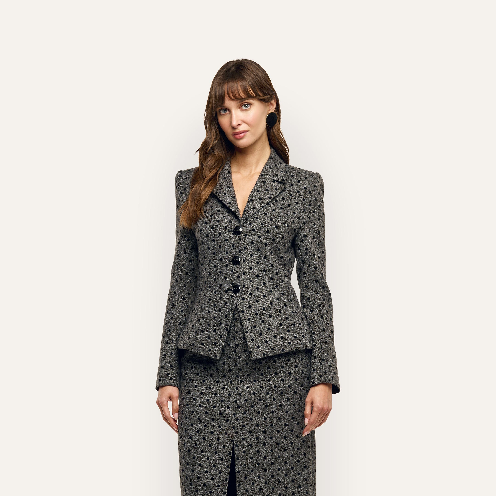 A person wears a tailored, velvet flocked grey Odile Blazer with black polka dots and a matching skirt.