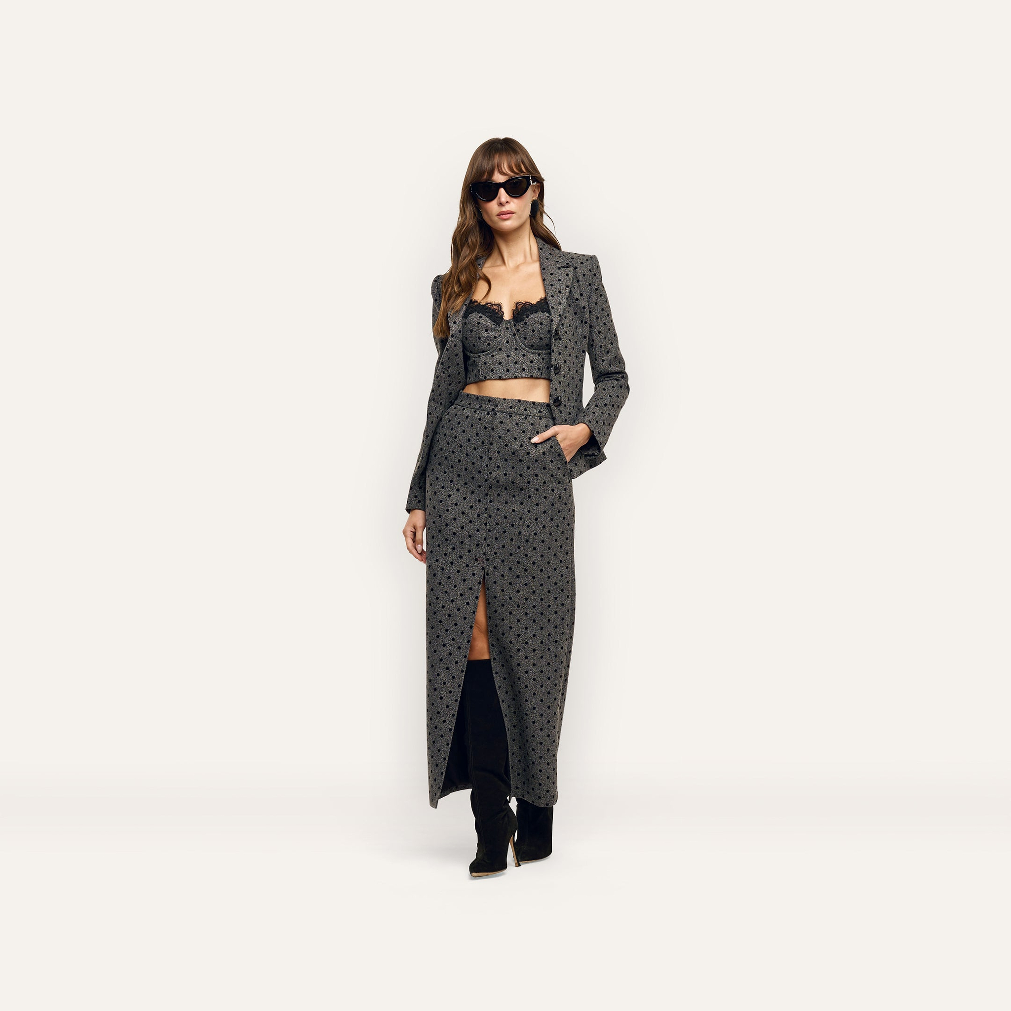 A woman wearing an Odile Blazer in fitted, velvet flocked polka-dot, with a matching lace-trimmed crop top and a long skirt with a front slit.