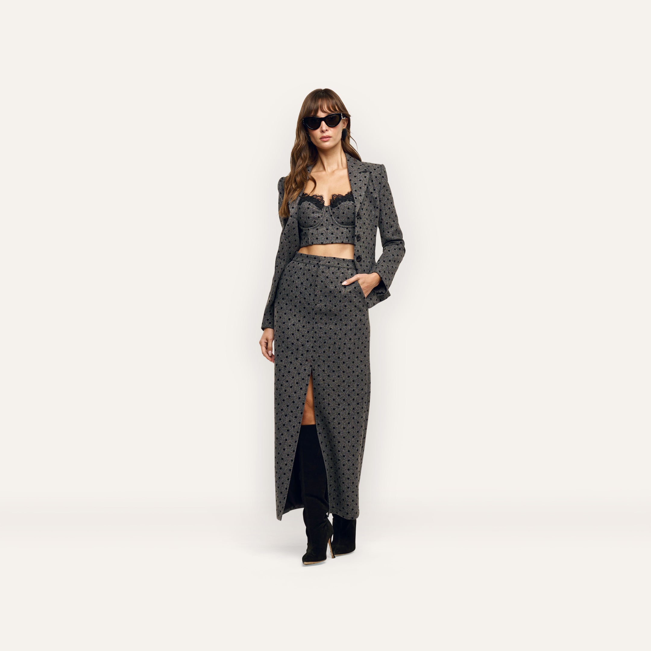 A woman wearing an Odile Blazer in fitted, velvet flocked polka-dot, with a matching lace-trimmed crop top and a long skirt with a front slit.