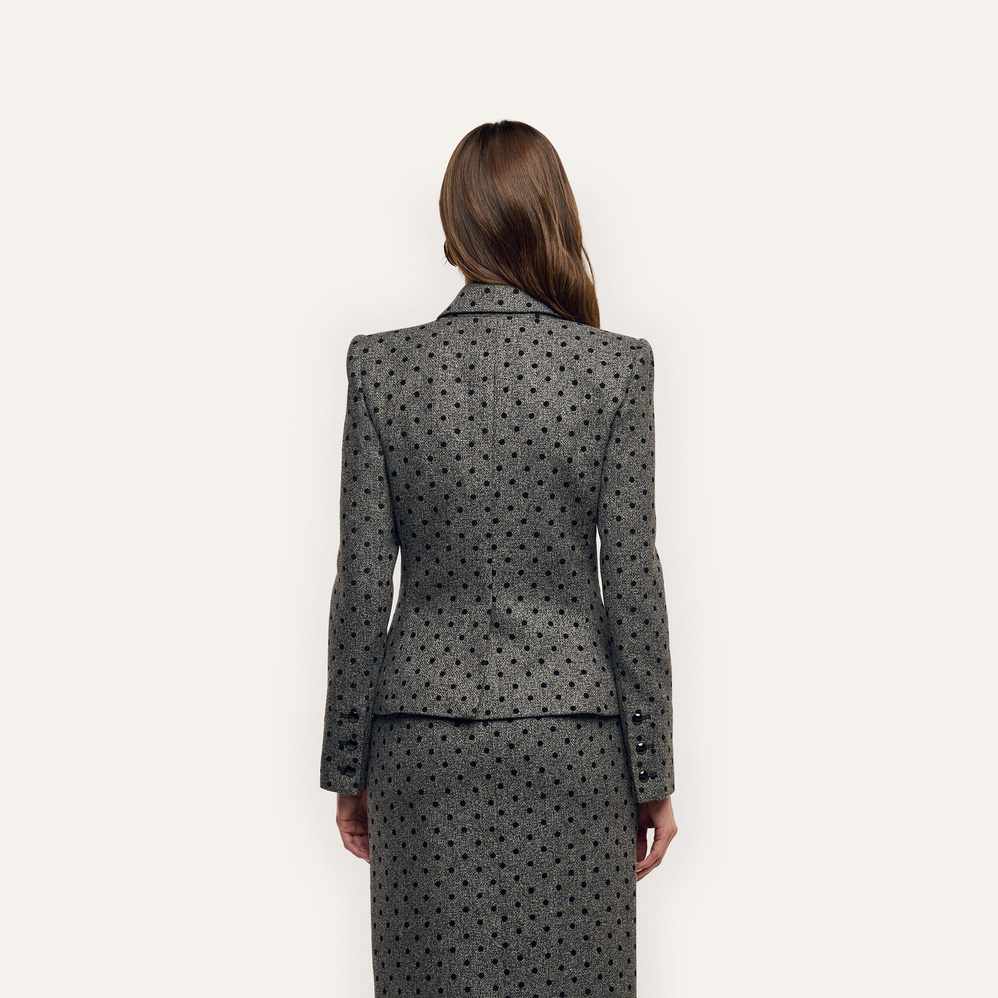 A person viewed from behind wearing a grey polka-dot Odile Blazer with notched lapels and a matching skirt.