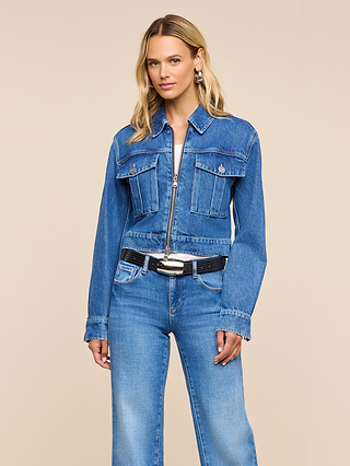 Wearing the Micah Oversized Jean Jacket and jeans, a person with long blonde hair, accessorized with a black belt and large hoop earrings, stands against a plain beige background.