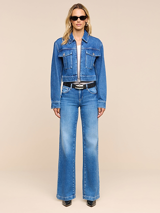 A person wearing the Micah Oversized Jean Jacket, paired with matching flared jeans, a black belt, black pointed shoes, and sunglasses, stands facing forward against a plain beige background.