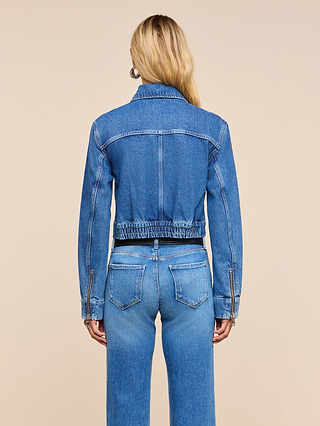 A person with long blonde hair wears the Micah Oversized Jean Jacket and blue jeans, seen from the back against a plain beige background.