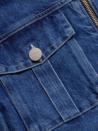Close-up of the Micah Oversized Jean Jacket in blue indigo denim, featuring a textured pocket with a metal button inscribed “LAMOUR.” A visible zipper runs along the top edge, showcasing the classic style and fabric detail characteristic of this statement jacket.
