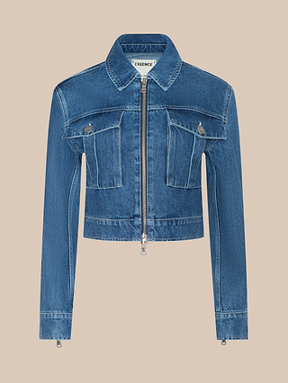 The Micah Oversized Jean Jacket in blue is displayed on a plain beige background, showcasing its cropped design with a front zipper, pointed collar, long sleeves, and two chest flap pockets.