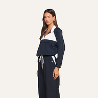 A woman wears the Vex Cropped Windbreaker, a navy blue and white long-sleeve activewear jacket, paired with matching drawstring pants while standing against a plain background.