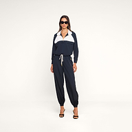 A woman stands confidently against a plain white background, hands in her pockets and wearing sunglasses, styled in the Vex Cropped Windbreaker and black heels.