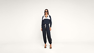 A woman wearing sunglasses and a navy blue tracksuit with white accents stands confidently in heels against a plain white background.