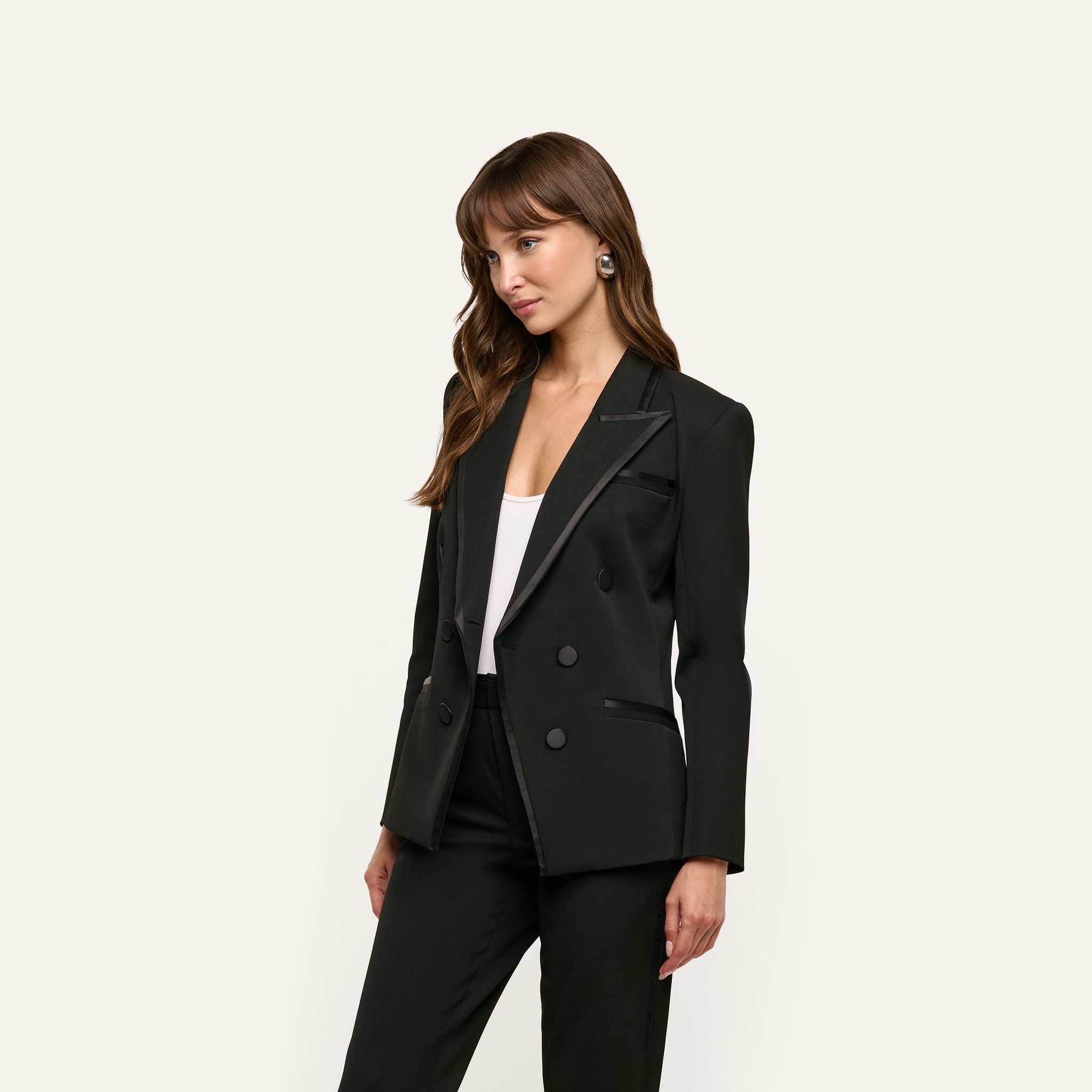 A woman wears a black Kyomi Double-Breasted Blazer in stretch suit fabric with satin lapel detailing over a white top.