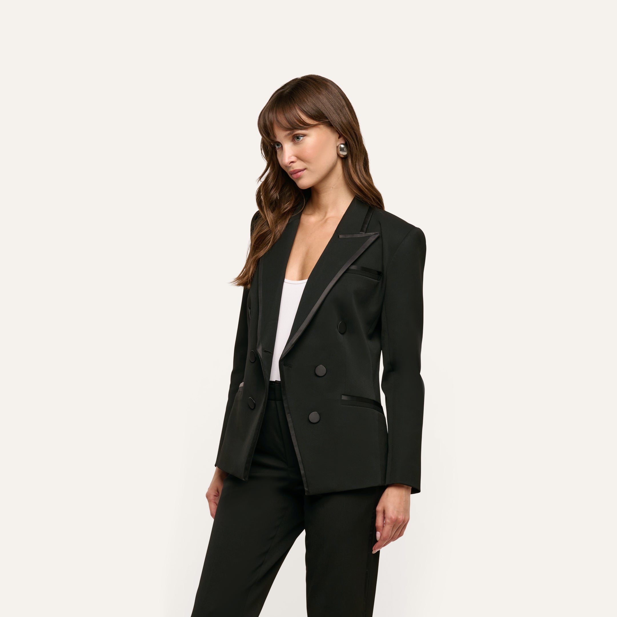 A woman wears a black Kyomi Double-Breasted Blazer in stretch suit fabric with satin lapel detailing over a white top.