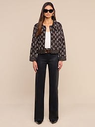 Una donna con indosso occhiali da sole, la giacca in pelle decorata Morrisa con motivo nero, un top bianco, pantaloni neri a gamba larga e scarpe nere è ritratta di fronte, su uno sfondo beige a tinta unita.