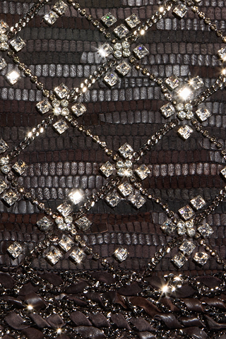 Close-up of the Morrisa Embellished Leather Jacket reveals a dark, textured recycled leather surface with a reptile-inspired pattern, intricately hand-embellished with a crisscross grid of sparkling rhinestones and metallic chains set in diamond shapes—each element catching the light for an unforgettable statement look.