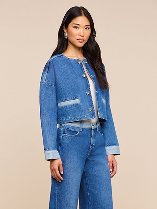 A woman with long dark hair wears the Verona Jean Jacket and high-waisted blue jeans as she stands against a beige background.