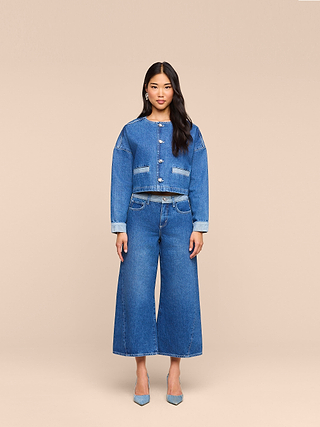 A woman stands facing forward, wearing the Arabell Romper from L’AGENCE. She has long dark hair and is styled with gray pointed-toe heels. The background is plain beige, creating a clean backdrop for this warm weather essential look.