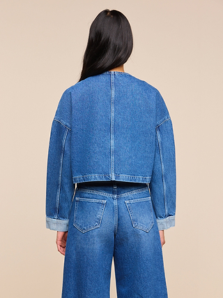 A person with long dark hair, seen from behind, is wearing the oversized Verona Jean Jacket and high-waisted blue jeans against a plain beige background.
