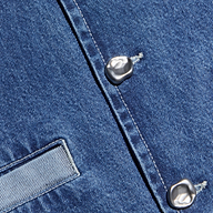 Close-up of blue denim fabric from the Verona Jean Jacket, featuring two silver buttons and a rectangular stitched pocket, highlighting the material’s texture and stitching details.