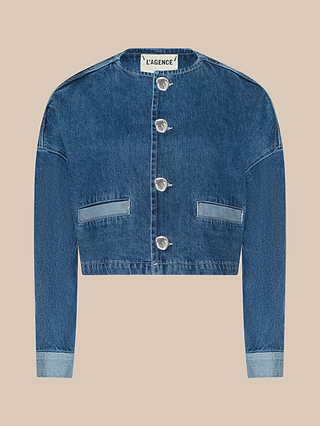 The Verona Jean Jacket, a cropped blue collarless denim piece with long sleeves, large silver buttons, and two front pockets, is displayed on a beige background.