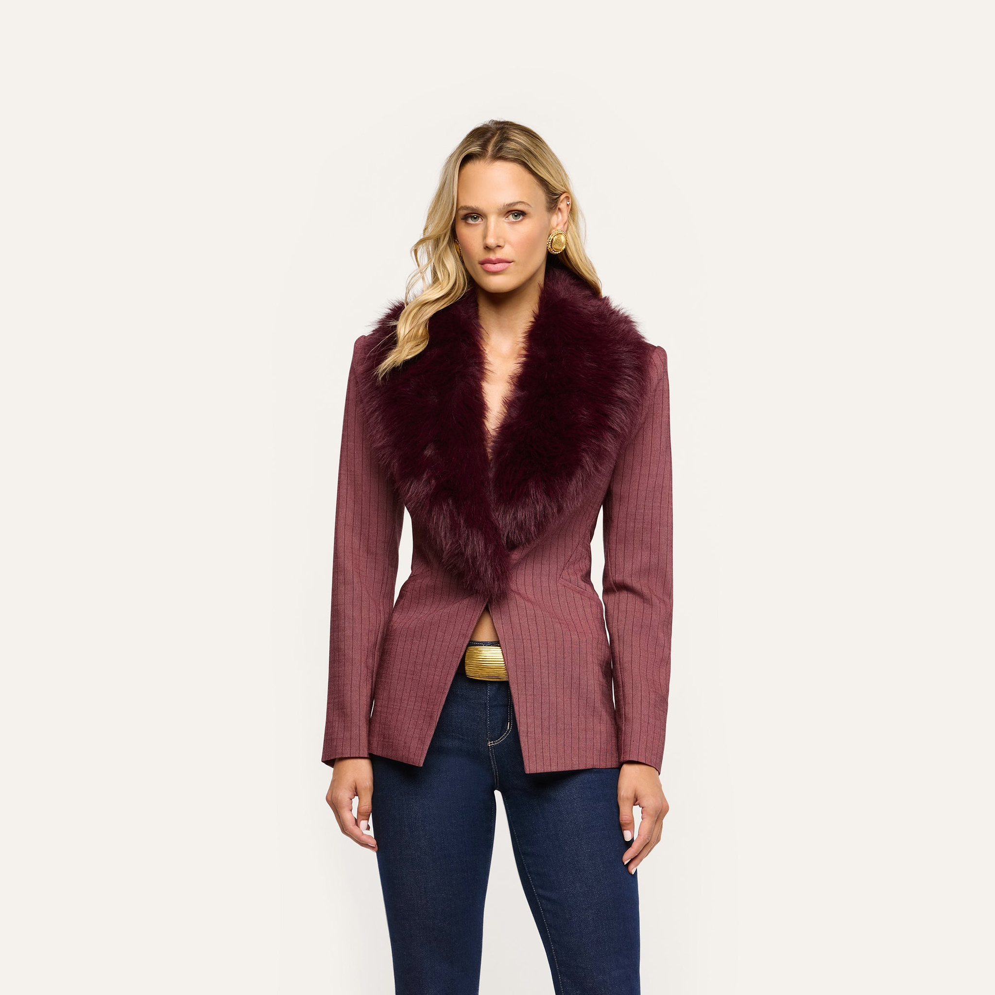 A woman wears a burgundy pinstriped Sheila Blazer with a large faux-fur collar over dark blue jeans.