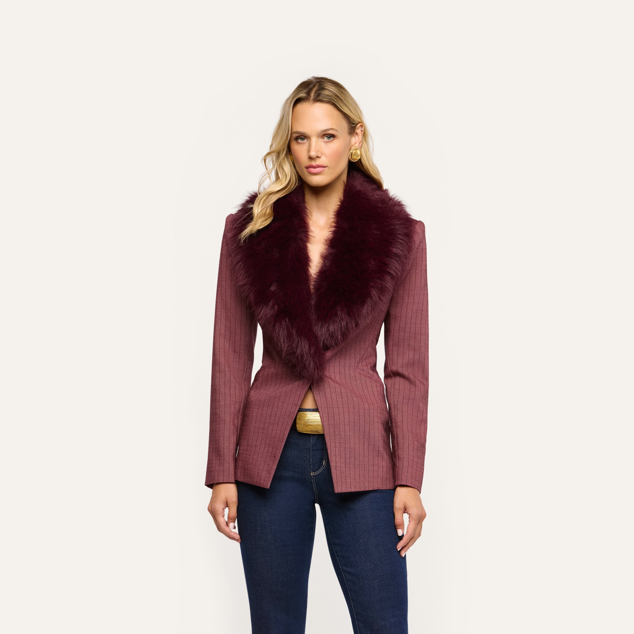 A woman wears a burgundy pinstriped Sheila Blazer with a large faux-fur collar over dark blue jeans.