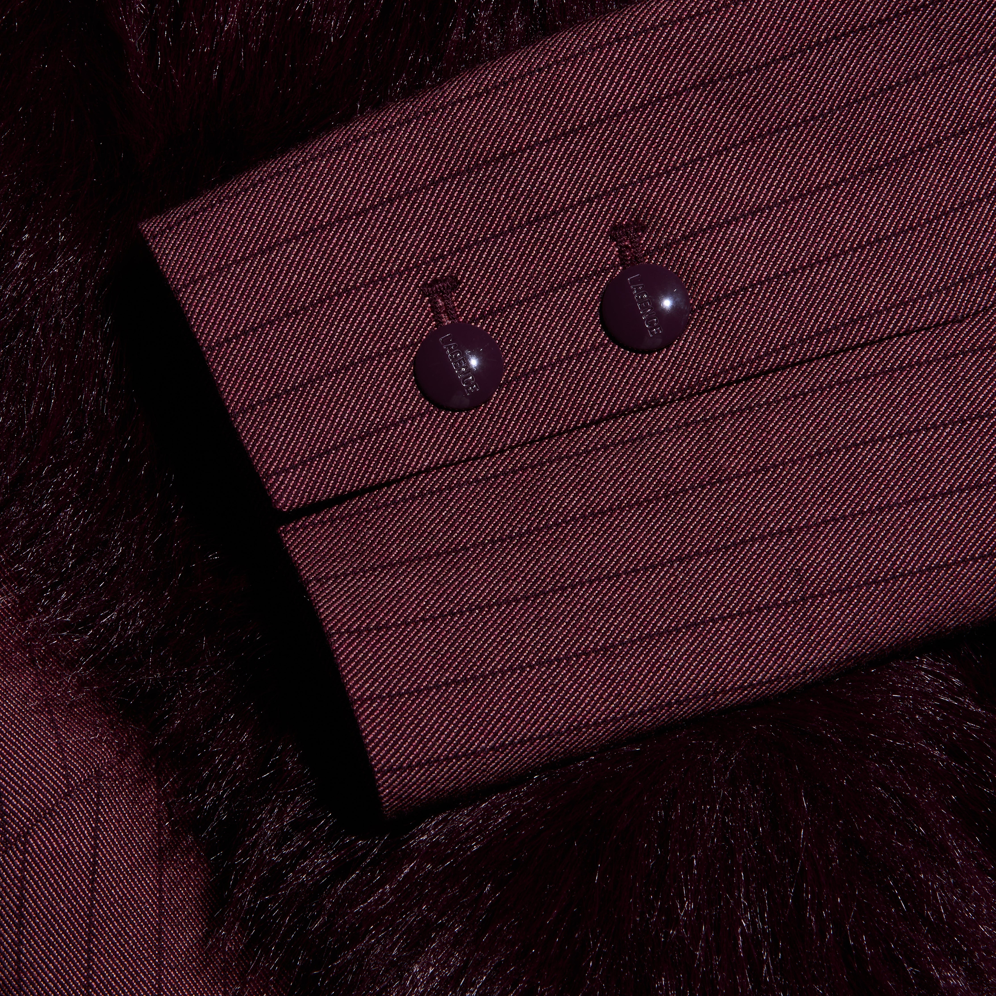 A close-up of a Sheila Blazer burgundy pinstripe sleeve cuff with two matching buttons against a dark, faux fur collar.