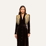 A woman stands against a plain light background, wearing the Garavani Crystal Cape—a long, dark velvet coat featuring gold beaded fringe on the shoulders and a satin collar.