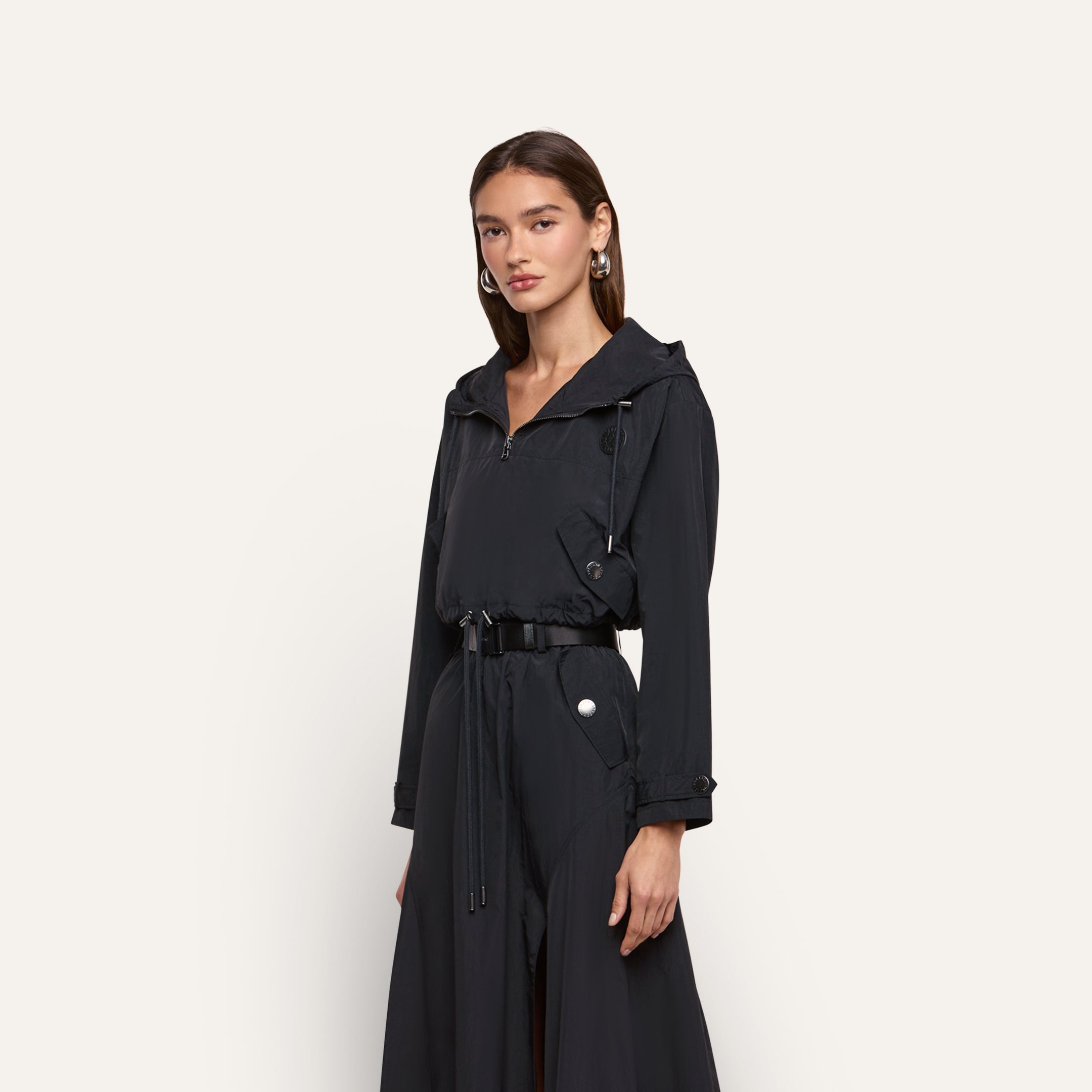 A person wears a black water-repellant Derby Windbreaker with a quarter-zip front and a black belt at the waist.