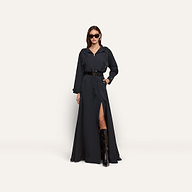 A person wearing a black Derby Windbreaker dress featuring a belted waist, front zipper, and thigh-high slit, paired with knee-high boots and sunglasses.