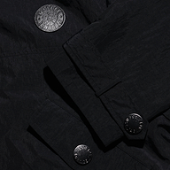 Close-up of a black, water-repellant Derby Windbreaker featuring textured fabric, a circular patch with a lion emblem, and metallic button fasteners.