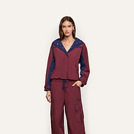 A woman wears a burgundy Geovana Windbreaker with a navy blue collar, hood, and sleeve panels, paired with matching cargo pants.