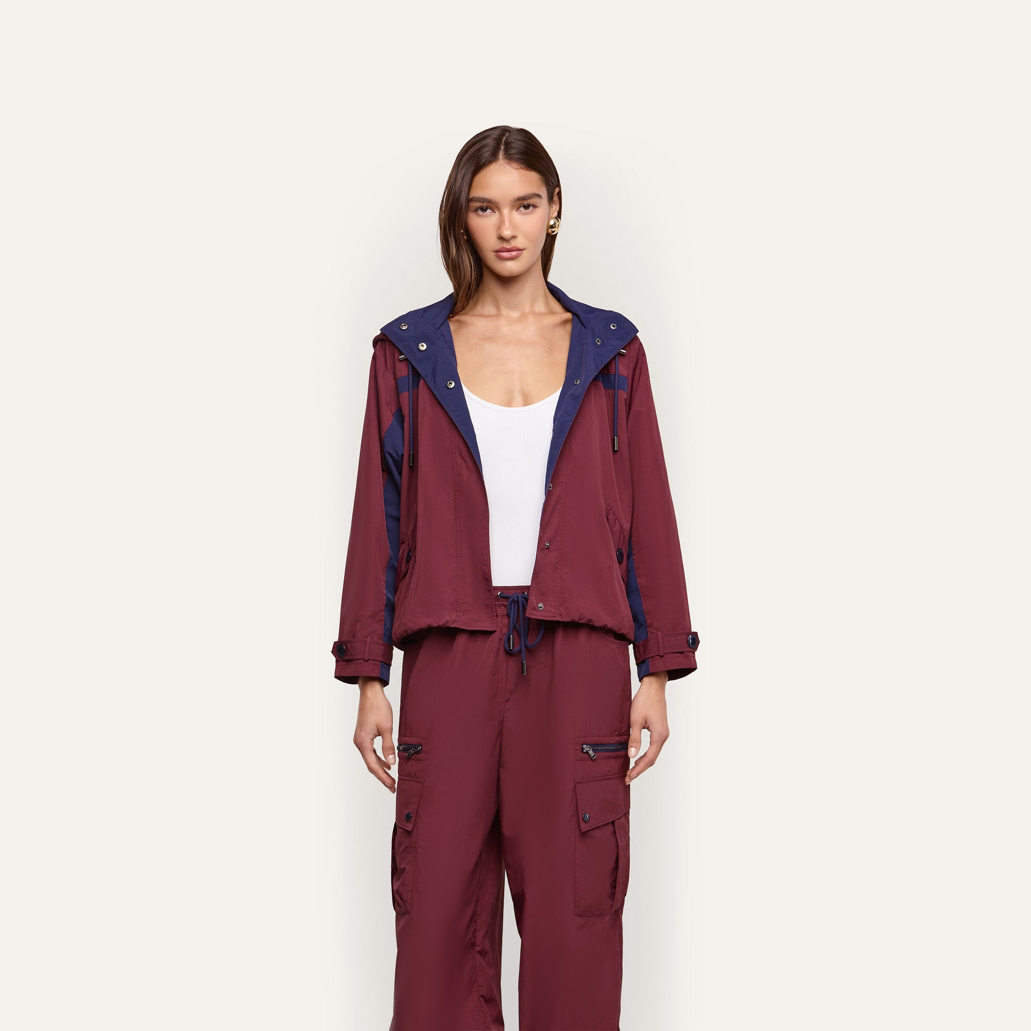 A model wears a maroon Geovana Windbreaker with blue accents and matching drawstring cargo pants over a white tank top, making it a travel must-have.