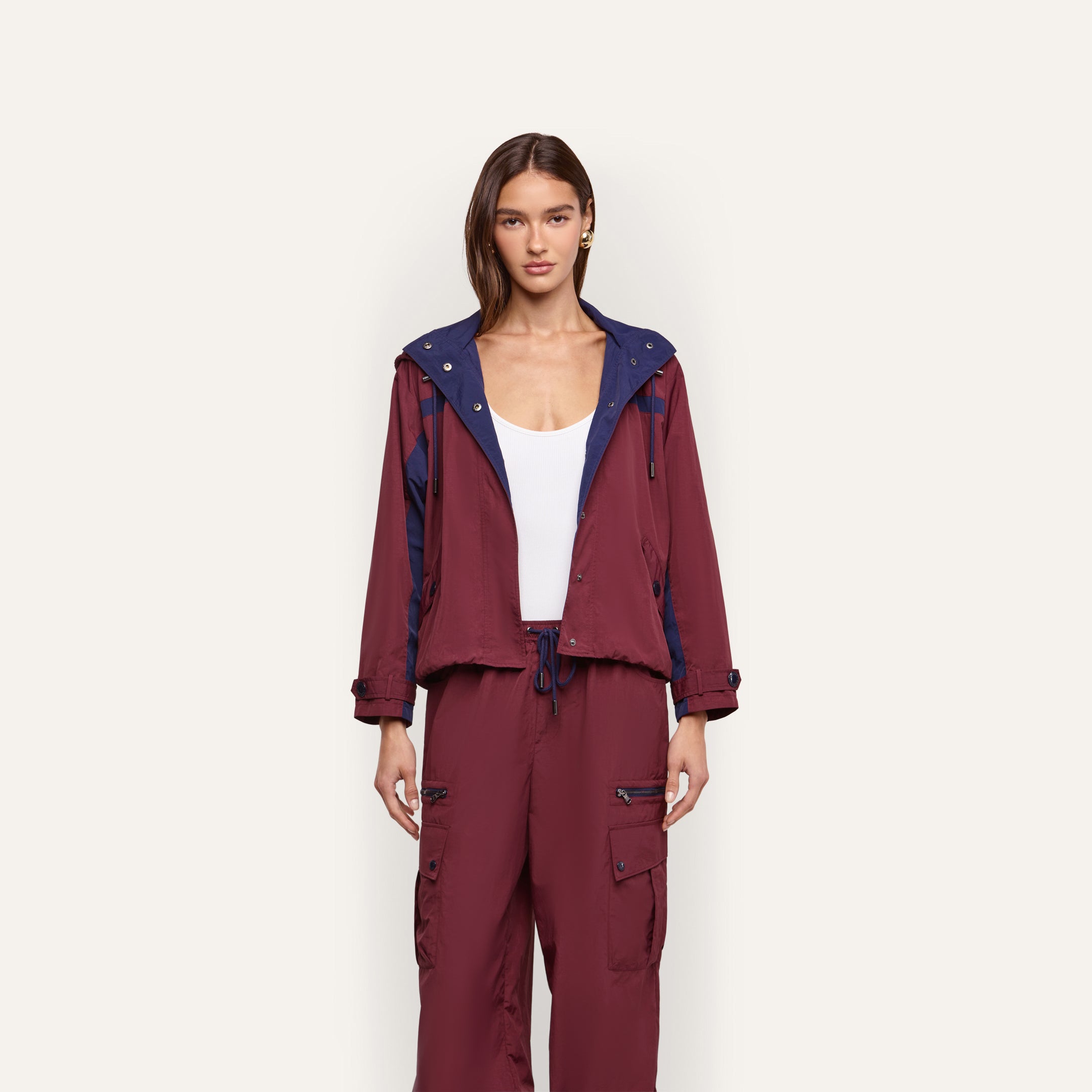 A model wears a maroon Geovana Windbreaker with blue accents and matching drawstring cargo pants over a white tank top, making it a travel must-have.