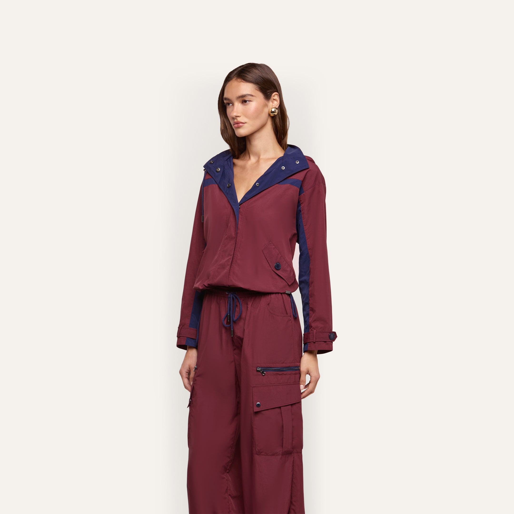 A person wearing a maroon and dark blue Geovana Windbreaker with matching cargo pants.