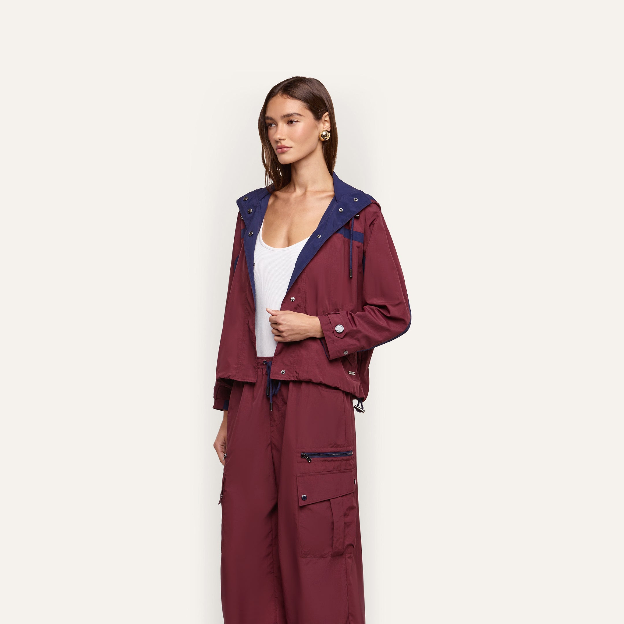 A person wears a maroon Geovana Windbreaker with a navy blue collar and matching high-waisted cargo pants over a white tank top.