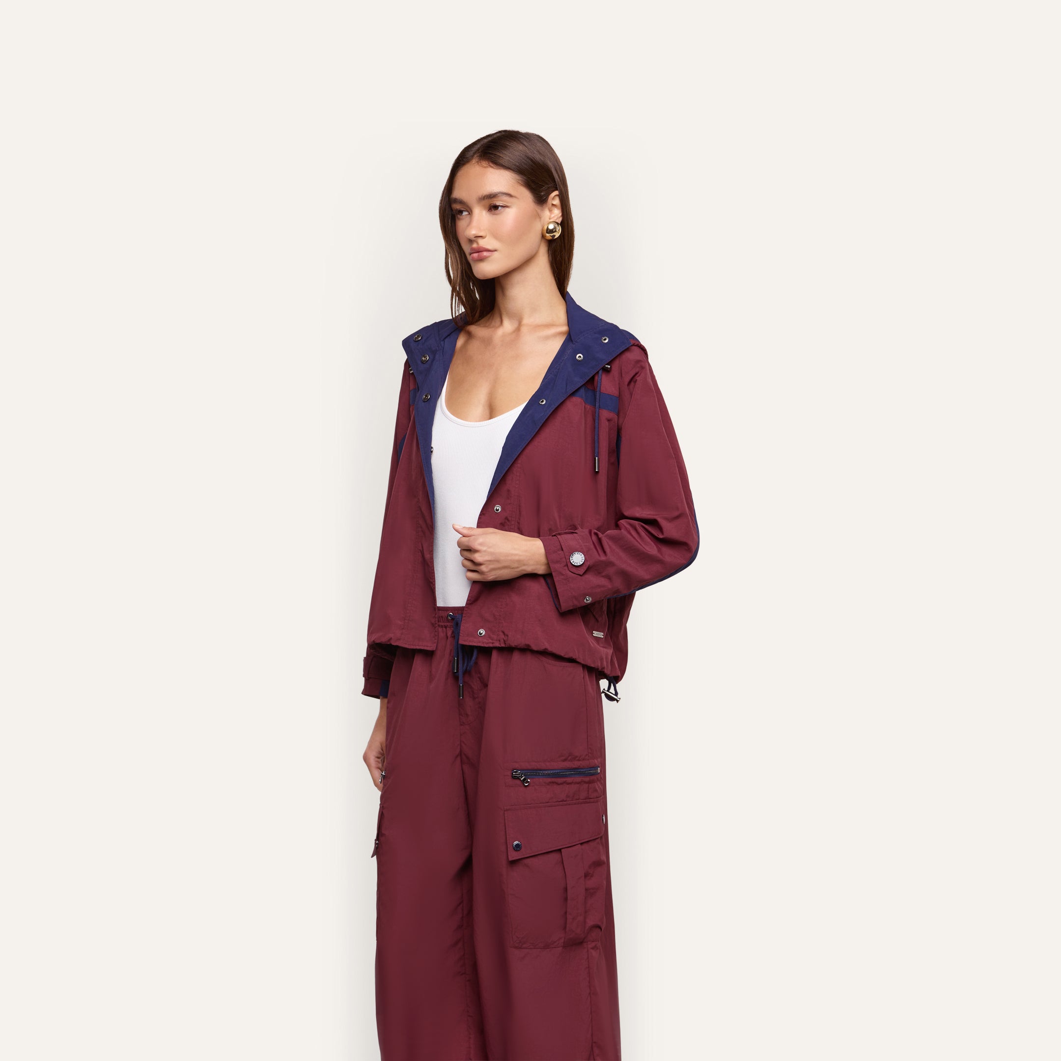 A person wears a maroon Geovana Windbreaker with a navy blue collar and matching high-waisted cargo pants over a white tank top.