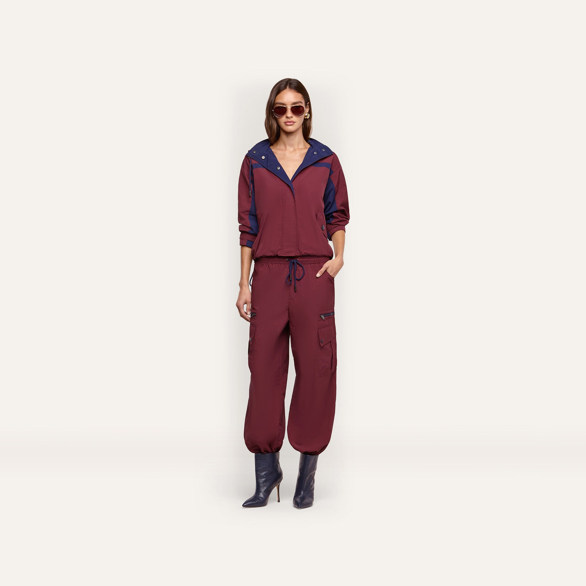 A person wearing a maroon Geovana windbreaker with blue collar trim and matching maroon cargo-style joggers with a drawstring waist.