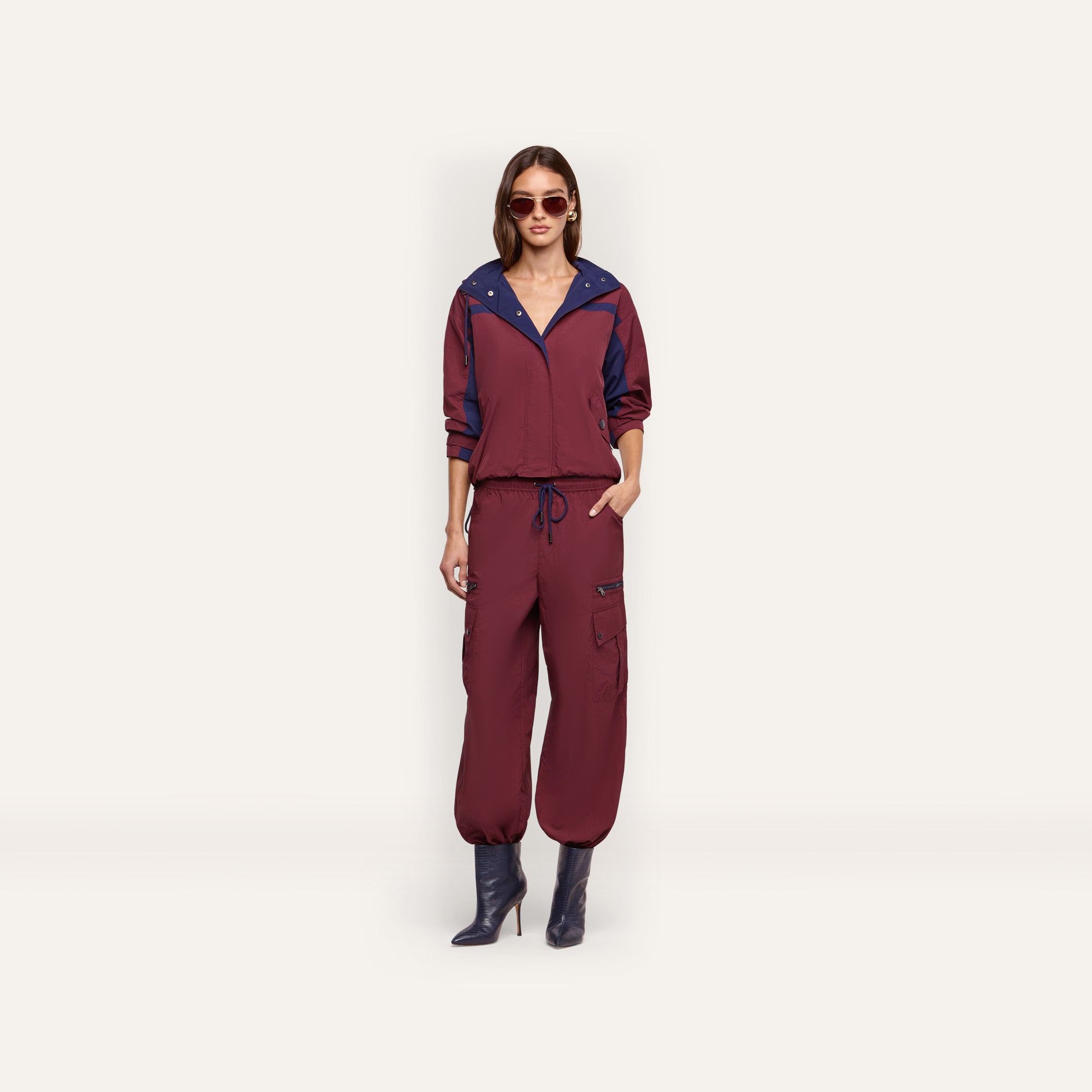 A person wearing a maroon Geovana windbreaker with blue collar trim and matching maroon cargo-style joggers with a drawstring waist.