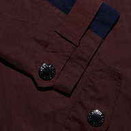 Maroon Geovana windbreaker sleeve featuring a dark blue cuff accent, a strap with a black button, and a large black button on the water-repellant pocket.