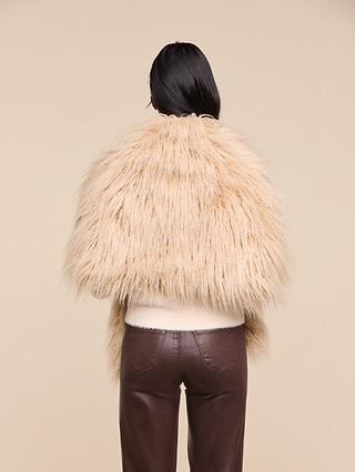 A person with long dark hair, seen from behind, wears a beige faux fur jacket styled with the Sabine Faux Fur Scarf and dark brown leather pants against a plain beige background—a perfect cool-weather accessory for a special event.