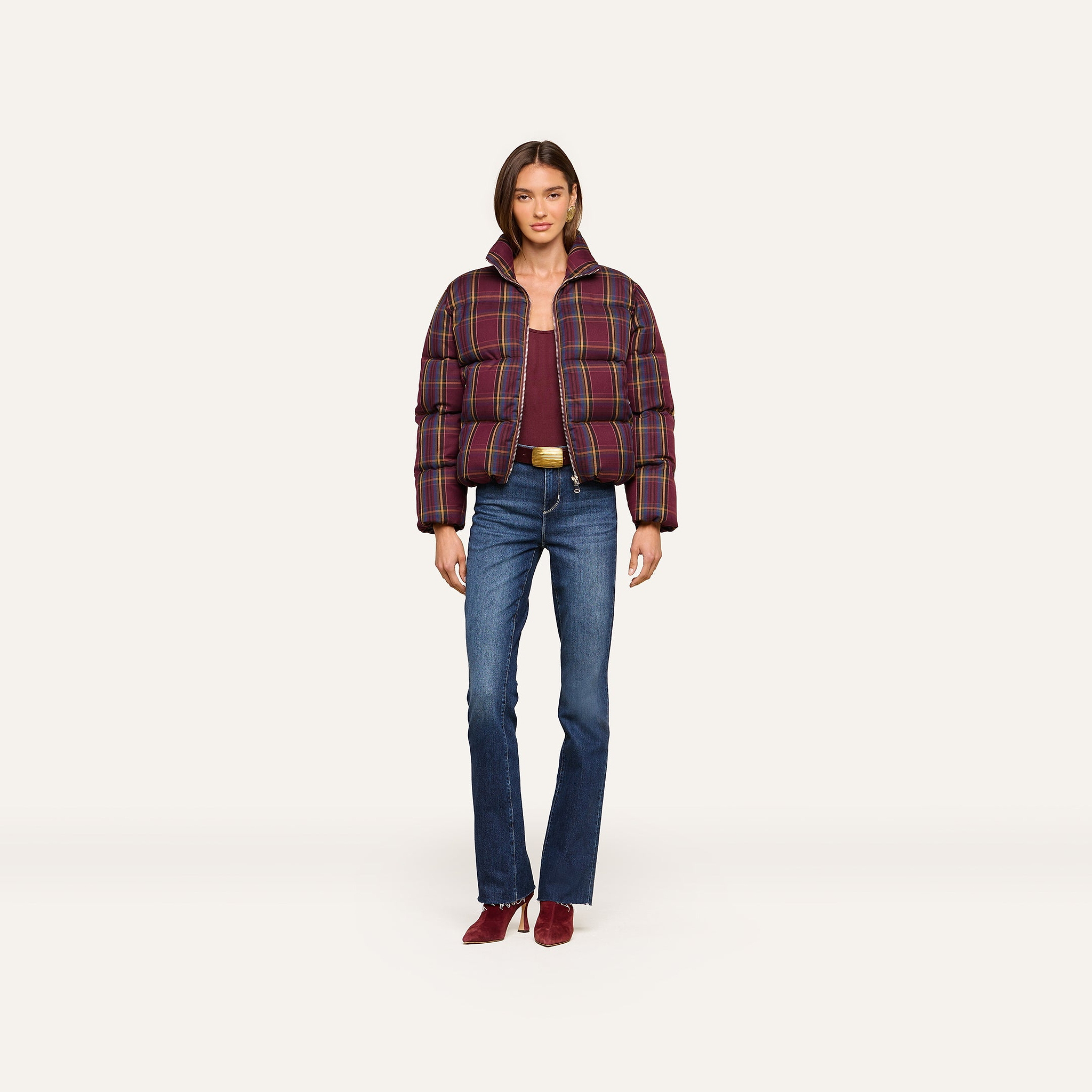 A woman stands facing forward against a plain light background, wearing the Larsa Oversized Puffer Jacket over a maroon top, blue jeans, and maroon shoes.