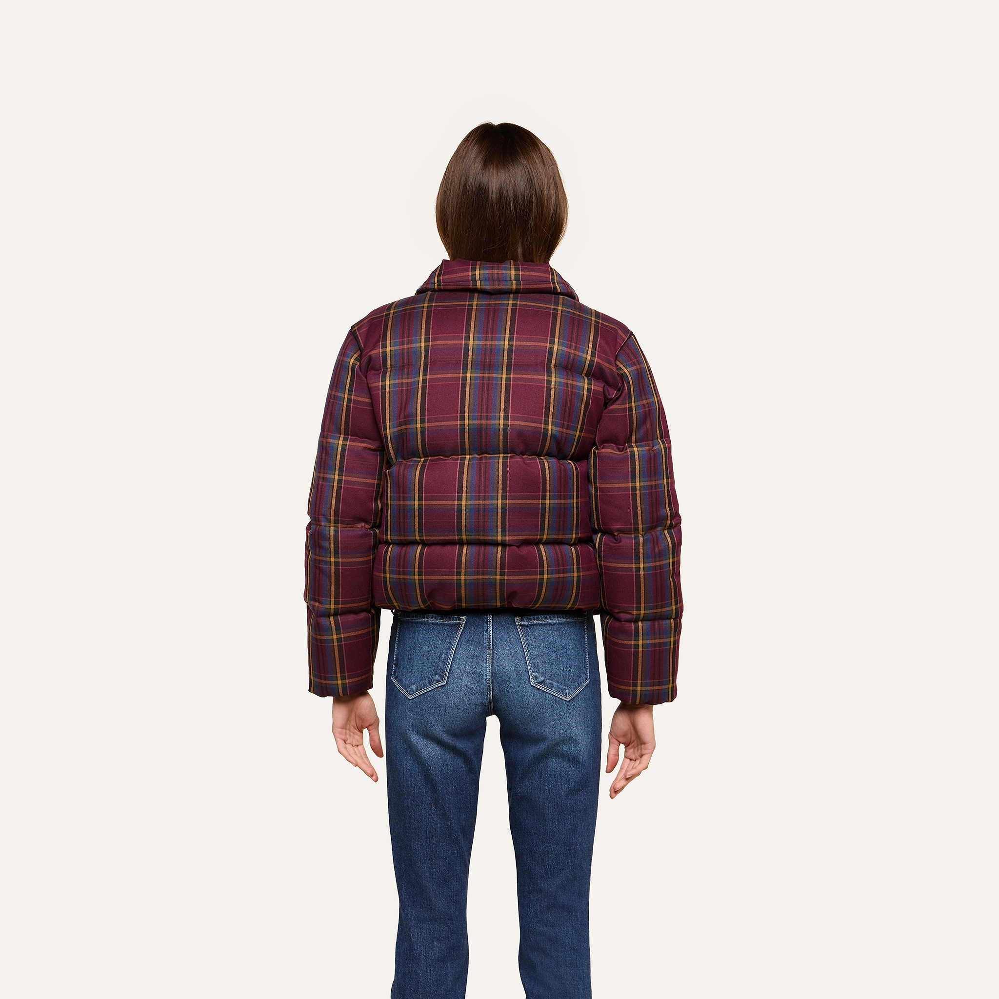A person stands facing away, wearing the Larsa Oversized Puffer Jacket in a red and yellow plaid pattern with blue jeans against a plain light background.