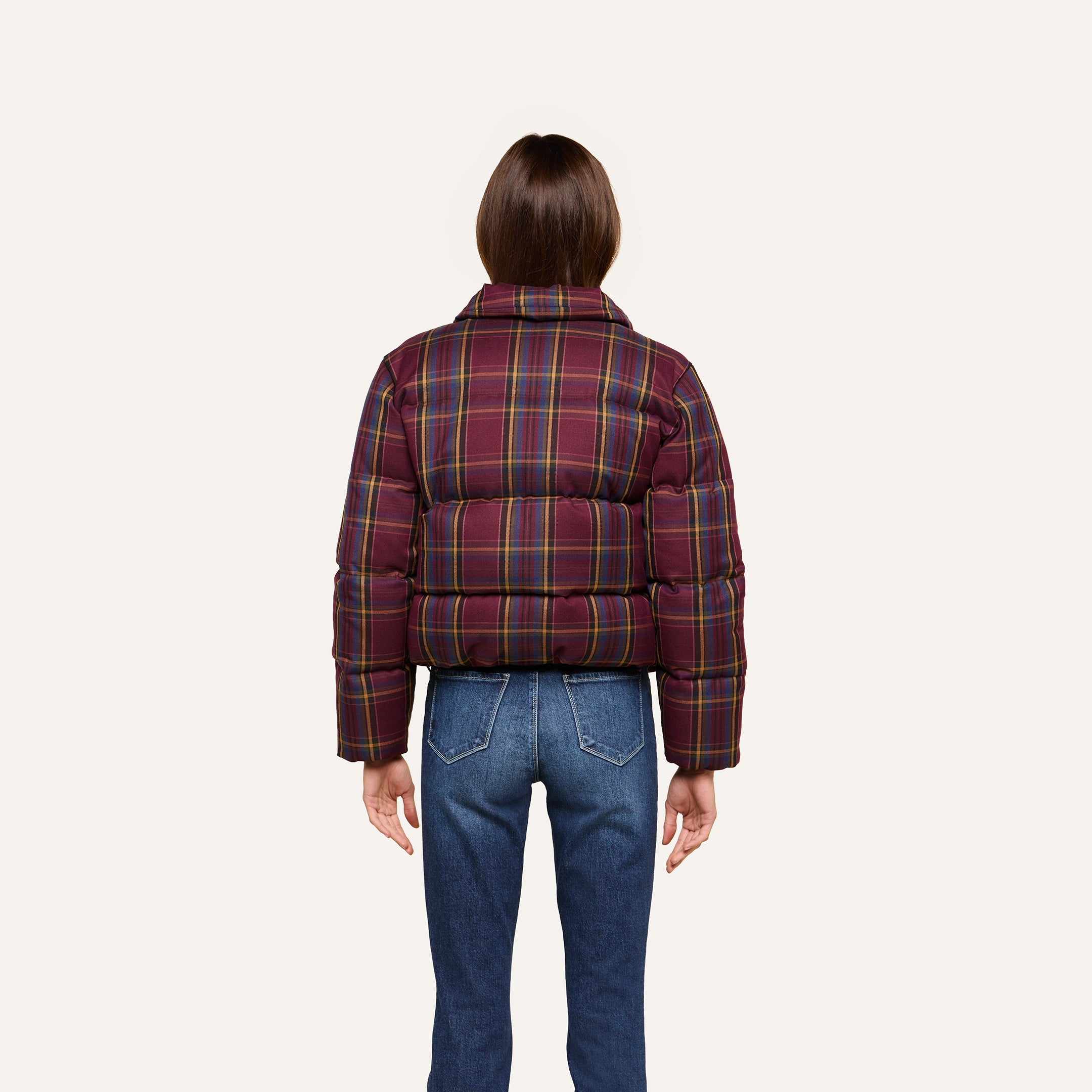 A person stands facing away, wearing the Larsa Oversized Puffer Jacket in a red and yellow plaid pattern with blue jeans against a plain light background.