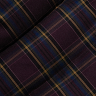 The Larsa Oversized Puffer Jacket features dark purple tartan fabric with intersecting lines in gold, black, and blue, creating a classic plaid pattern. The soft woven texture recalls traditional plaid materials, with two sections of the fabric slightly overlapping at an angle.