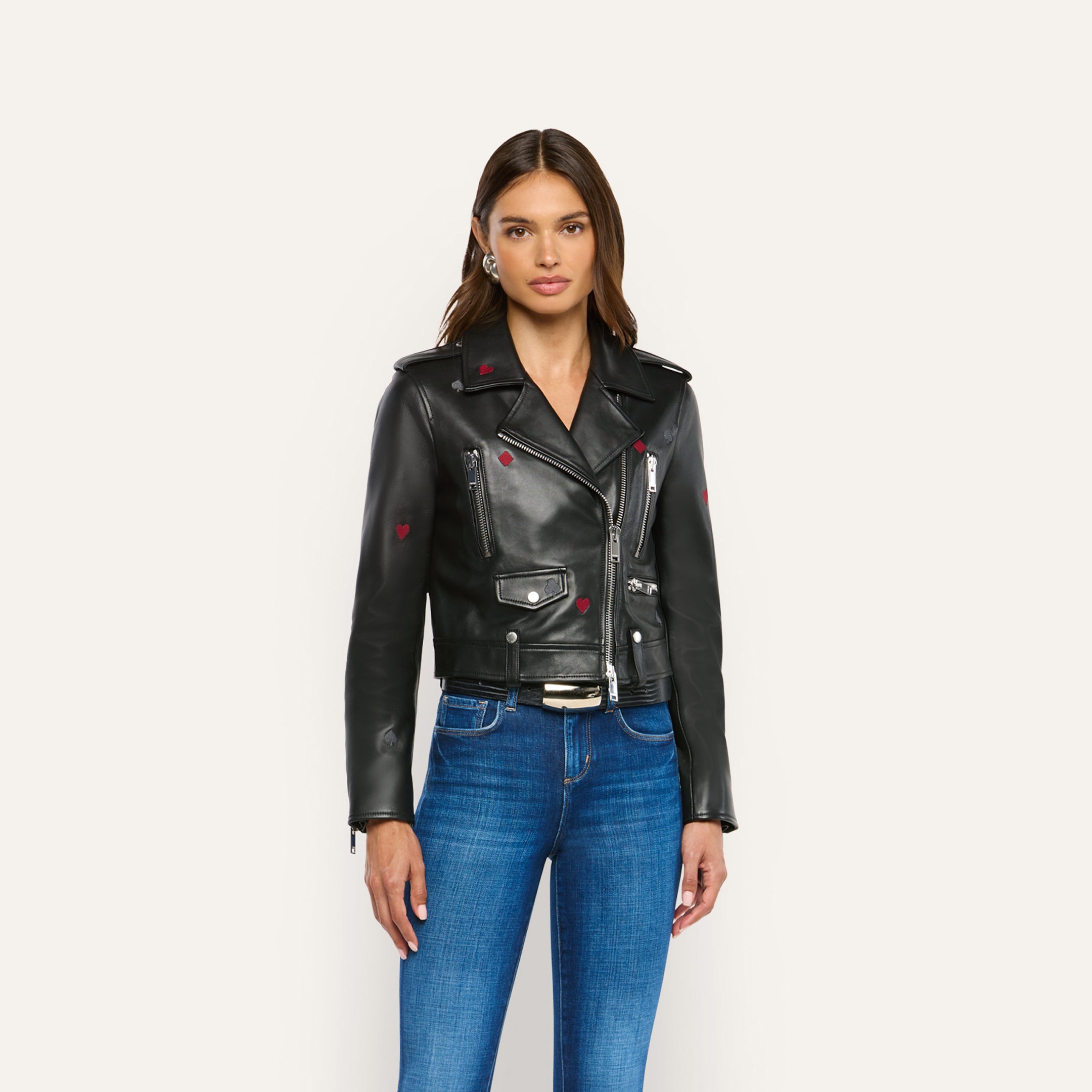 A woman wears a Blakely Embroidered Leather Jacket featuring small red heart details with blue jeans.